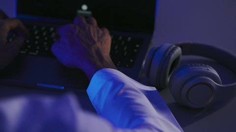 الاستفادة من التكنولوجيا الحديثة، مفهوم الإصغاء والاستماع، تصوير مقرب ليد لرجل عربي خيجي سعودي يستخدم الحاسب المحمول و بجانبه سماعة الرأس، النقر على لوحة المفاتيح