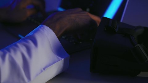 استخدام الأجهزة التكنولوجية والتقنيات الحديثة, محاكاة العالم الخيالي, صورة مقربة لرجل عربي خليجي إماراتي يقوم بإنجاز العمل على الحاسوب المحمول وبجانبه نظارة الفي ار, شاب سعودي يمتلك مهارة الكتابة السريعة على الكيبورد