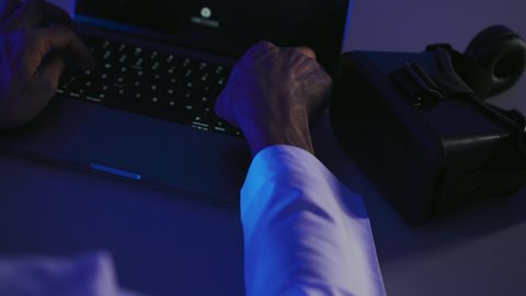 محاكاة العالم الخيالي، استخدام الأجهزة التكنولوجية والتقنيات الحديثة, صورة مقربة لرجل عربي خليجي إماراتي يقوم بإنجاز العمل على الحاسوب المحمول وبجانبه نظارة الفي ار, شاب سعودي يمتلك مهارة الكتابة السريعة على الكيبورد