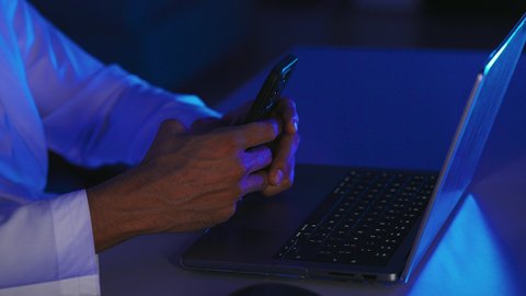 Browsing social media sites, mobile phone services and applications, technological development and progress, modern and advanced technical devices, a close-up shot of the hand of an Arab Gulf Saudi man sitting in front of a laptop using a mobile phone.