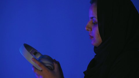 قضاء أوقات ممتعة بسماع الاغاني والمقاطع الصوتية، استعمال تقنية الهيدفون، مفهوم الإصغاء والاستماع، شابة سعودية تستخدام التكنولوجيا الحديثة،تصوير مقرب من الجانب لامرأة عربية خيجية سعودية  ترتدي العباءة تقوم بيدها سماعة الرأس