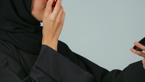 أدوات تجميل نسائيه عصريه، التسويق لمنتجات التجميل, بورتريه مقرب من الجانب لفتاه عربيه سعودية خليجيه ترتدي الحجاب و العباءة تقوم بوضع توريد الخدود, مفهوم الانوثه والاهتمام بالمظهر الخارجي, مكياج وميكاب تتوريال, صالون نسائي راقي, خلفيه رمادي