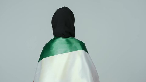 الاعتزاز بالراية العمانية، المشاركة بالاحتفال بذكرى اليوم الوطني، إيماءات الفخر بالانتماء للبلاد، بورتريه لمهندسة عربية خليجية عمانية ترتدي الحجاب والعباءة السوداء وسترة الحماية  تحمل علم السلطنة على كتفها، خلفية رمادية