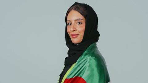 المشاركة بالاحتفال بذكرى اليوم الوطني، الاعتزاز بالراية العمانية، إيماءات الفخر بالانتماء للبلاد، بورتريه لمهندسة عربية خليجية عمانية ترتدي الحجاب والعباءة السوداء وسترة الحماية  تحمل علم السلطنة على كتفها، خلفية رمادية