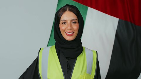 بورتريه  لمهندسة عربية خليجية عمانية ترتدي الحجاب والعباءة السوداء وسترة الحماية تقف وبخلفها علم سلطنة عمان ، تقديم التحية بإيماءات الفخر بالانتماء للبلاد، الاحتفال بذكرى اليوم الوطني، الاعتزاز بالراية العمانية، خلفية علم السلطنة