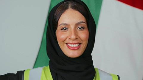 تقديم التحية بإيماءات الفخر بالانتماء للبلاد، الاحتفال بذكرى اليوم الوطني، الاعتزاز بالراية العمانية، بورتريه  لمهندسة عربية خليجية عمانية ترتدي الحجاب والعباءة السوداء وسترة الحماية تقف وبخلفها علم سلطنة عمان ، خلفية علم السلطنة