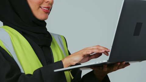 إدارة ومتابعة العمل، دمج التكنولوجيا الحديثة في القطاع الهندسي, متابعة المشاريع الإنشائية عبر الحاسوب المحمول, بورتريه لمهندسة عربية خليجية سعودية ترتدي الحجاب والعباءة السوداء تقوم بالتعديل على مخطط الإعمار عن طريق التطبيقات والمواقع الهندسية, خلفية رمادية