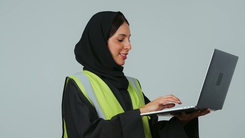 دمج التكنولوجيا الحديثة في القطاع الهندسي, متابعة المشاريع الإنشائية عبر الحاسوب المحمول, بورتريه لمهندسة عربية خليجية سعودية ترتدي الحجاب والعباءة السوداء تقوم بالتعديل على مخطط الإعمار عن طريق التطبيقات والمواقع الهندسية, إدارة ومتابعة العمل، خلفية رمادية