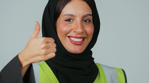 العمل في القطاع الهندسي, مفهوم الهندسة والانشاءات المعمارية، الجودة الفنية في تقنية التصميم والبناء،مهن ووظائف نسائية, بورتريه لمهندسة عربية خليجية سعودية ترتدي الحجاب والعباءة السوداء ترفع يدها بإيماءات الاعجاب والقبول, خلفية رمادية