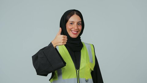مفهوم الهندسة والانشاءات المعمارية، الجودة الفنية في تقنية التصميم والبناء، العمل في القطاع الهندسي, مهن ووظائف نسائية, بورتريه لمهندسة عربية خليجية سعودية ترتدي الحجاب والعباءة السوداء ترفع يدها بإيماءات الاعجاب والقبول, خلفية رمادية