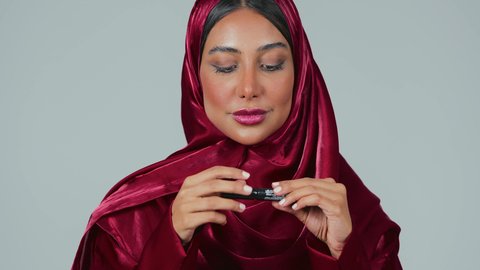 خبيرة مستحضرات التجميل النسائية، استخدام الماسكرا لإبراز جمال العينين، الإهتمام بالجمال والمظهر الخارجي، دورات تعليمية لمكياج تتوريال,بورتريه لسيدة عربية خليجية سعودية سمراء ترتدي العباءة والحجاب تقوم بوضع الميكاب، خلفيه رمادية