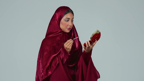 دورات مكياج تدريبية ، الإهتمام بالجمال والمظهر الخارجي ، التسويق لمنتجات التجميل، بورتريه لامراة عربية خليجية سعودية سمراء ترتدي العباءة والحجاب تستخدم  فرشاة ظل العيون ، خلفية رمادية