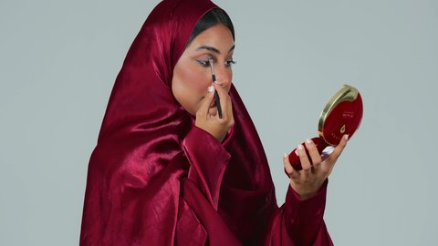 بورتريه لامراة عربية خليجية سعودية سمراء ترتدي العباءة والحجاب تستخدم  فرشاة ظل العيون ، أدوات مكياج تتوريال ، الإهتمام بالجمال والمظهر الخارجي ، التسويق لمنتجات التجميل،خلفية رمادية