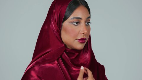 مفهوم التزين والتجمل, التسويق لمنتجات ومستحضرات التجميل, الاناقة والاهتمام بالجمال والمظهر الخارجي, بورتريه لامرأة عربية خليجية سعودية سمراء ترتدي العباءة والحجاب تقوم بوضع الرموش الاصطناعية, خلفية رمادية