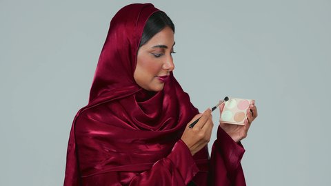 بورتريه لامراة عربية خليجية سعودية سمراء ترتدي العباءة والحجاب تستخدم  فرشاة ظل العيون ، أدوات مكياج تتوريال ، الإهتمام بالجمال والمظهر الخارجي ، التسويق لمنتجات التجميل، خلفية رمادية