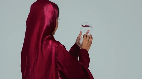 مفهوم الانوثة والنعومة , الاهتمام والعناية بالبشرة والجمال, الشغف بوضع المكياج,  بورتريه لسيدة عربية خليجية سعودية سمراء ترتدي العباءة والحجاب تمسك بيديها علبة وفرشاة أحمر الخدود, النظر إلى الكاميرا بإيماءات السعادة والسرور, خلفية رمادية