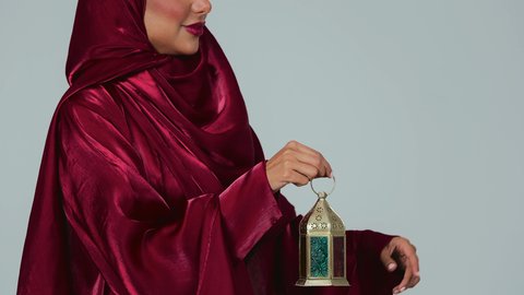 أجواء رمضانية مبهجة ، أعياد ومناسبات اسلامية ، شهر رمضان المبارك، بورتريه لسيدة عربية خليجية سعودية سمراء ترتدي العباءة والحجاب تمسك فانوس رمضان، خلفية رمادية