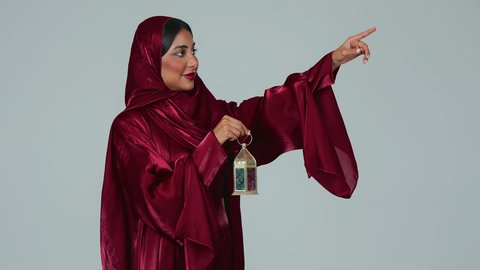 بورتريه لسيدة عربية خليجية سعودية سمراء ترتدي العباءة والحجاب تمسك فانوس رمضان، أجواء رمضانية مبهجة ، أعياد ومناسبات اسلامية ، شهر رمضان المبارك، خلفية رمادية