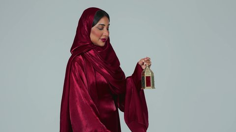 شهر رمضان المبارك، أعياد ومناسبات اسلامية ، بورتريه لسيدة عربية خليجية سعودية سمراء ترتدي العباءة والحجاب تمسك فانوس رمضان، أجواء رمضانية مبهجة ، خلفية رمادية