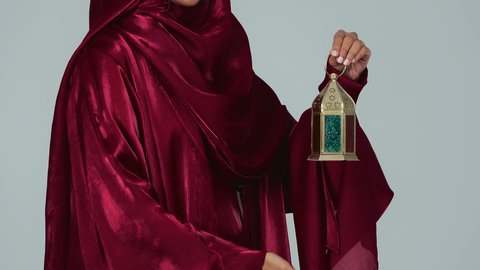 أعياد ومناسبات اسلامية ، شهر رمضان المبارك، بورتريه لسيدة عربية خليجية سعودية سمراء ترتدي العباءة والحجاب تمسك فانوس رمضان، أجواء رمضانية مبهجة ، خلفية رمادية