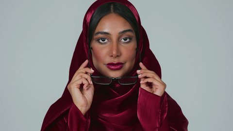 المحافظة على صحة العينين، مفهوم تحسين وتعديل الرؤية،ارتداء النظارات الخاصة بضعف النظر، بورتريه لسيدة عربية خليجية سعودية سمراء ترتدي العباءة والحجاب تقوم بوضع النظاره الطبيه ، خلفية رمادية