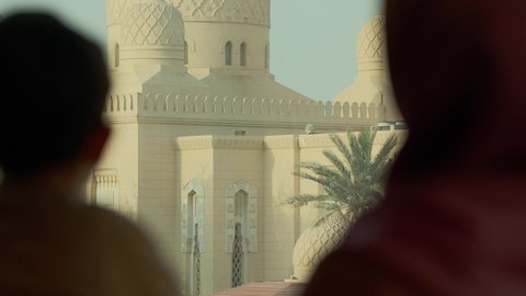 تأمل معالم الوطن، الفن الهندسي المعماري للمساجد في الإمارات، أماكن لأداء العبادة والتقرب إلى الله تعالى، تصوير مقرب من الخلف لولد عربي خليجي اماراتي يرتدي الكندورة يقف مع والدته يقومان بالنظر إلى المسجد