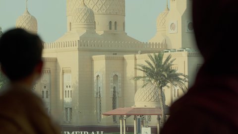 The architectural art of mosques in the UAE, places for worship and getting closer to Allah Almighty, reflecting the landmarks of the homeland, a close-up shot from behind of an Emirati Gulf Arab boy wearing a kandura standing with his mother as they look at the mosque.
