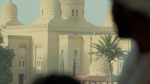 سارية علم الامارات ترفرف في سماء الوطن، الفن الهندسي المعماري للمساجد في الإمارات، أماكن لأداء العبادة والتقرب إلى الله تعالى، تصوير مقرب من الخلف لرجل عربي خليجي اماراتي يرتدي الكندورة والغترة يقف مع ابنه ويقوم بالنظر إلى المسجد