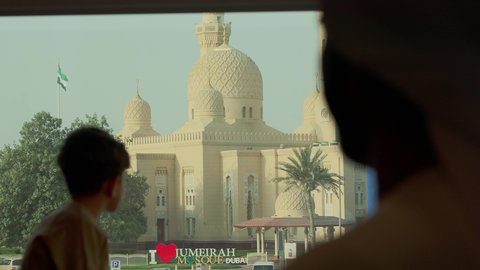 The architectural art of mosques in the UAE, places for worship and getting closer to God Almighty, elegance and attention to the exterior appearance, a close-up shot from behind of an Arab Gulf Emirati man wearing the kandura and the Emirati ghutrah standing with his son and looking at the mosque.