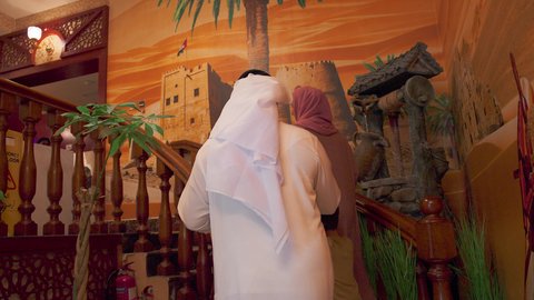 قضاء الأوقات الممتعة مع الابناء, تقديم الاهتمام والعناية للاولاد، أنشطة ترفيهية مسلية, الاستمتاع بالأجواء العائلية في الخارج, عائلة عربية خليجية اماراتية يرتدون الزي التقليدي الاماراتي يصعدون على سلم خشبي في إحدى المطاعم الفاخرة