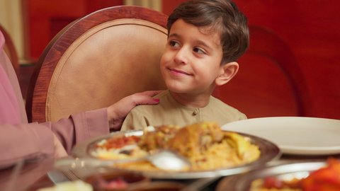 العناية وتقديم الاهتمام للاولاد، قضاء الأوقات الممتعة مع الابناء, مائدة مليئة بالاطباق والمأكولات الشعبية الشهية، أنشطة ترفيهية مسلية, الاستمتاع بالأجواء العائلية في الخارج, سيدة عربية خليجية اماراتية تقوم بإطعام ابنها في إحدى المطاعم