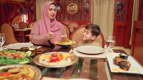 قضاء الأوقات الممتعة مع الابناء, مائدة مليئة بالاطباق والمأكولات الشعبية الشهية، أنشطة ترفيهية مسلية, الاستمتاع بالأجواء العائلية في الخارج, سيدة عربية خليجية اماراتية تقوم بإطعام ابنها في إحدى المطاعم