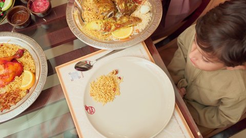 تقديم الاهتمام والعناية للاولاد، قضاء الأوقات الممتعة مع الابناء, مائدة مليئة بالاطباق والمأكولات الشعبية الشهية، أنشطة ترفيهية مسلية, الاستمتاع بالأجواء العائلية في الخارج, سيدة عربية خليجية اماراتية تقوم بإطعام ابنها في إحدى المطاعم