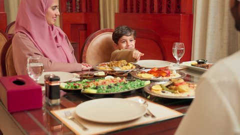 مائدة مليئة بالاطباق الشهية، مفهوم الأمان و الاستقرار العائلي, الاستمتاع بالأجواء العائلية في الخارج, أنشطة ترفيهية مسلية, قضاء الأوقات الممتعة مع الأسرة, عائلة عربية خليجية إماراتية يرتدون الزي التقليدي الإماراتي يجلسون على طاولة الطعام في إحدى المطاعم