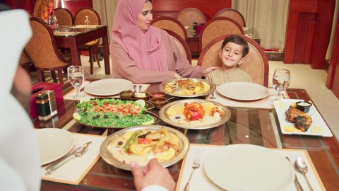 مائدة مليئة بالاطباق الشهية، مفهوم الأمان و الاستقرار العائلي, الاستمتاع بالأجواء العائلية في الخارج, أنشطة ترفيهية مسلية, قضاء الأوقات الممتعة مع الأسرة, عائلة عربية خليجية إماراتية يرتدون الزي التقليدي الإماراتي يجلسون على طاولة الطعام في إحدى المطاعم