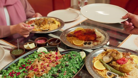 أنشطة ترفيهية مسلية, مائدة مليئة بالاطباق الشهية،  المحبة والمودة بين الزوجين, الاستمتاع بالأجواء العائلية في الخارج, قضاء الأوقات الممتعة مع الأسرة, زوجة عربية خليجية اماراتية تقوم بسكب طبق الطعام لزوجها في إحدى المطاعم