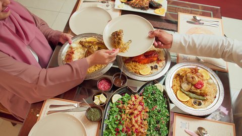 مائدة مليئة بالاطباق الشهية،  المحبة والمودة بين الزوجين, الاستمتاع بالأجواء العائلية في الخارج, قضاء الأوقات الممتعة مع الأسرة, أنشطة ترفيهية مسلية, زوجة عربية خليجية اماراتية تقوم بسكب طبق الطعام لزوجها في إحدى المطاعم