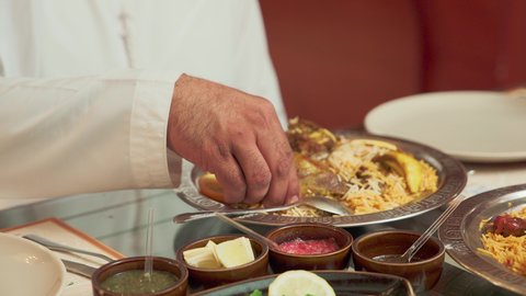 التلذذ بالمأكولات الشرقية ، تصوير  مقرب لرجل عربي خليجي اماراتي يتناول وجبة الغداء، طبق من أرز الكبسة و قطع لحم الحاشي المزين بالخضراوات و البقدونس، وصفات طعام المطبخ الاماراتي، مطاعم للمأكولات والوجبات العربية الشرقية.