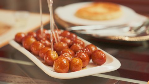 تناول الحلوى الشهية واللذيذة في احدى المطاعم، تصوير مقرب لطبق اللقيمات ذهبية اللون، حلا الزلابيات الشرقي المغموسة بالقطر، كرات العجين المقلية الصغيرة المرشوشة بالسمسم، الحلوى الشهية واللذيذة، وصفات وأطباق الحلويات والسكريات، ضيافة المناسبات والأعياد العربية