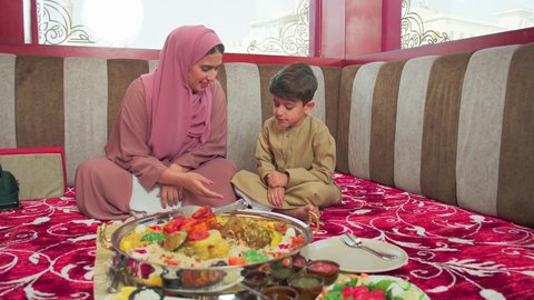 العناية والاهتمام بالابناء  ، مطاعم للمأكولات الشرقية ، فنون الطهي ووصفات طعام المطبخ الاماراتي،   منسف من الأرز الأبيض مع الدجاج المحمر والتوابل المزين بالخضراوات في احدى المطاعم الاماراتية ، ولد عربي اماراتي يرتدي الكندورة يقوم  بتناول اطباق شعبية شهية مع امه