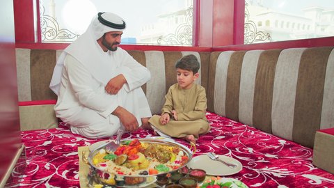 العناية والاهتمام بالابناء  ، مطاعم للمأكولات الشرقية ، فنون الطهي ووصفات طعام المطبخ الاماراتي،   منسف من الأرز الأبيض مع الدجاج المحمر والتوابل المزين بالخضراوات في احدى المطاعم الاماراتية ، ولد عربي اماراتي يرتدي الكندورة يقوم  بتناول اطباق شعبية شهية مع ابوه