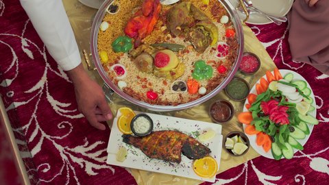 Traditional Arab dishes and meals, culinary arts and recipes of Emirati cuisine, restaurants for Eastern foods, an overhead shot of mansaf made with white rice, roasted chicken, and spices garnished with vegetables in one of the Emirati restaurants, a family enjoying delicious traditional dishes.