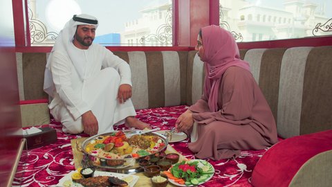 المحبة بين الزوجين  ، مطاعم للمأكولات الشرقية ، فنون الطهي ووصفات طعام المطبخ الاماراتي،   منسف من الأرز الأبيض مع الدجاج المحمر والتوابل المزين بالخضراوات في احدى المطاعم الاماراتية ، رجل عربي اماراتي يرتدي الكندورة و الغترة يقوم  بتناول اطباق شعبية شهية مع زوجته