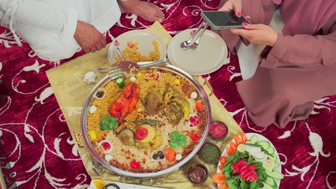 أطباق ووجبات عربية تقليدية ، فنون الطهي ووصفات طعام المطبخ الاماراتي، مطاعم للمأكولات الشرقية،  تصوير علوي لمنسف من الأرز الأبيض مع الدجاج المحمر والتوابل المزين بالخضراوات في احدى المطاعم الاماراتية ، عائلة تقوم بتناول اطباق شعبية شهية
