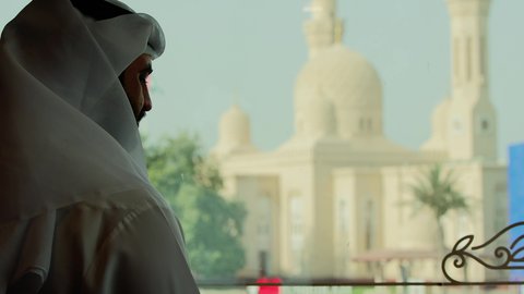 Elegance and attention to appearance, mosques for worship and getting closer to God Almighty, a close-up side shot of an Emirati Gulf Arab man wearing the kandura and Emirati ghutrah looking at the mosque.
