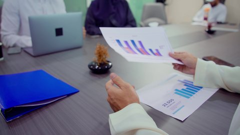 تبادل أوراق البيانات الإحصائية, عقد صفقات جديدة ، دمج الأجهزة التقنية الحديثة بالأعمال المكتبية، تطوير المشاريع و الاستثمارات، إدارة و تقسيم المهام، شرح و تحليل الرسوم البيانية, فريق عمل عربي خليجي اماراتي يقوم بإجراء اجتماع عمل داخل غرفة الاجتماعات في مقر الشركة