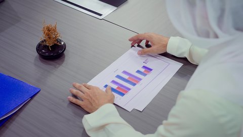 الاناقة والرجولة, مهام مكتبية في شركات الامارات العربية المتحدة، تصوير مقرب لايدي رجل عربي خليجي اماراتي يرتدي الكندورة والغترة البيضاء يدرس الرسوم البيانية، إنجاز مهام العمل عن بعد، إدارة شؤون الأعمال وتنظيمها عبر اللابتوب، خلفية ابراج وناطحات سحاب