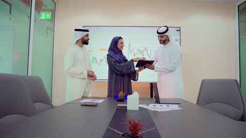 The use of modern and advanced technologies, integrating modern technical devices with office work, developing projects and investments, managing and dividing tasks, explaining and analyzing charts, a Gulf Arab Emirati team is holding a business meeting inside the conference room at the company's headquarters.