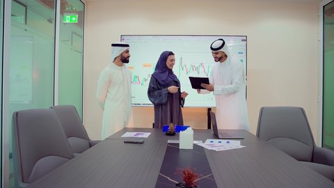 الحوار والنقاش بين الزملاء لإدارة الأعمال وتنظيمها، دمج الأجهزة التقنية الحديثة بالأعمال المكتبية، تطوير المشاريع و الاستثمارات، إدارة و تقسيم المهام، شرح و تحليل الرسوم البيانية, فريق عمل عربي خليجي اماراتي يقوم بإجراء اجتماع عمل داخل غرفة الاجتماعات في مقر الشركة