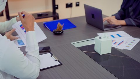 Analysis and study of statistical data sheets, integrating modern technical devices with office work, developing projects and investments, managing and dividing tasks, explaining and analyzing charts, a Gulf Arab Emirati team is holding a business meeting in the company's conference room.